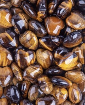 A pile of shiny, golden tiger eye crystals heart, each one with a distinct striped pattern.