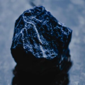 A photograph of a beautiful sodalite crystal on a dark background. The crystal is a deep, rich blue color.